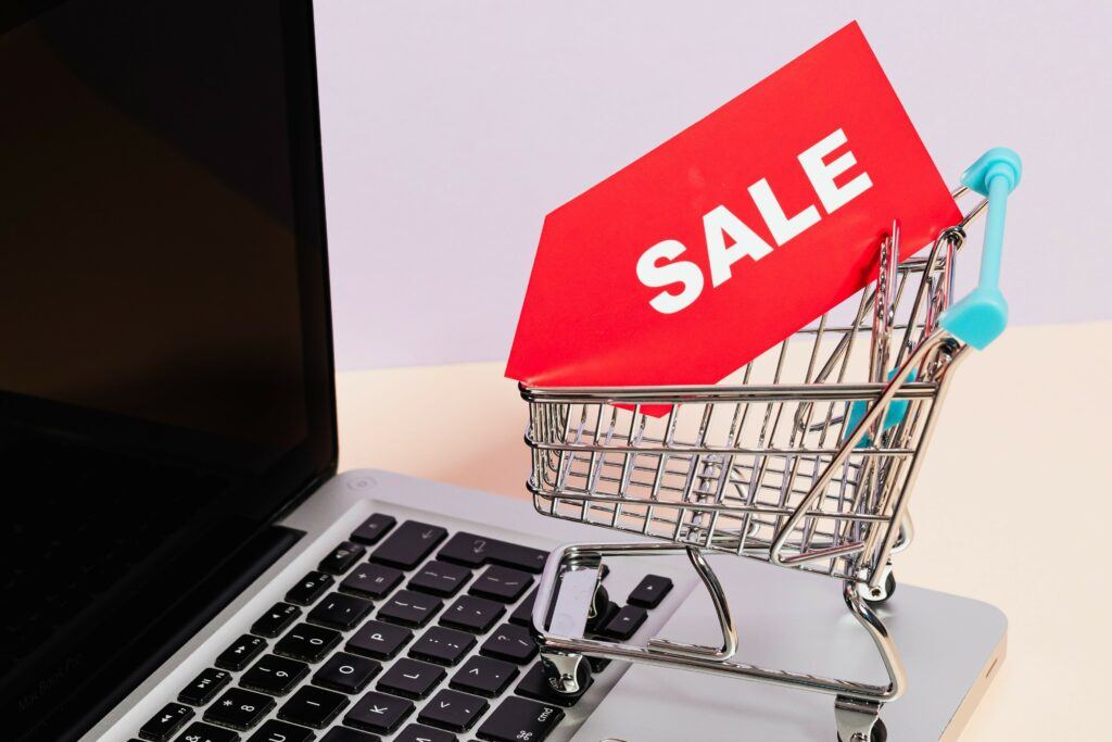 Mini shopping basket with sale sticker on top of laptop.